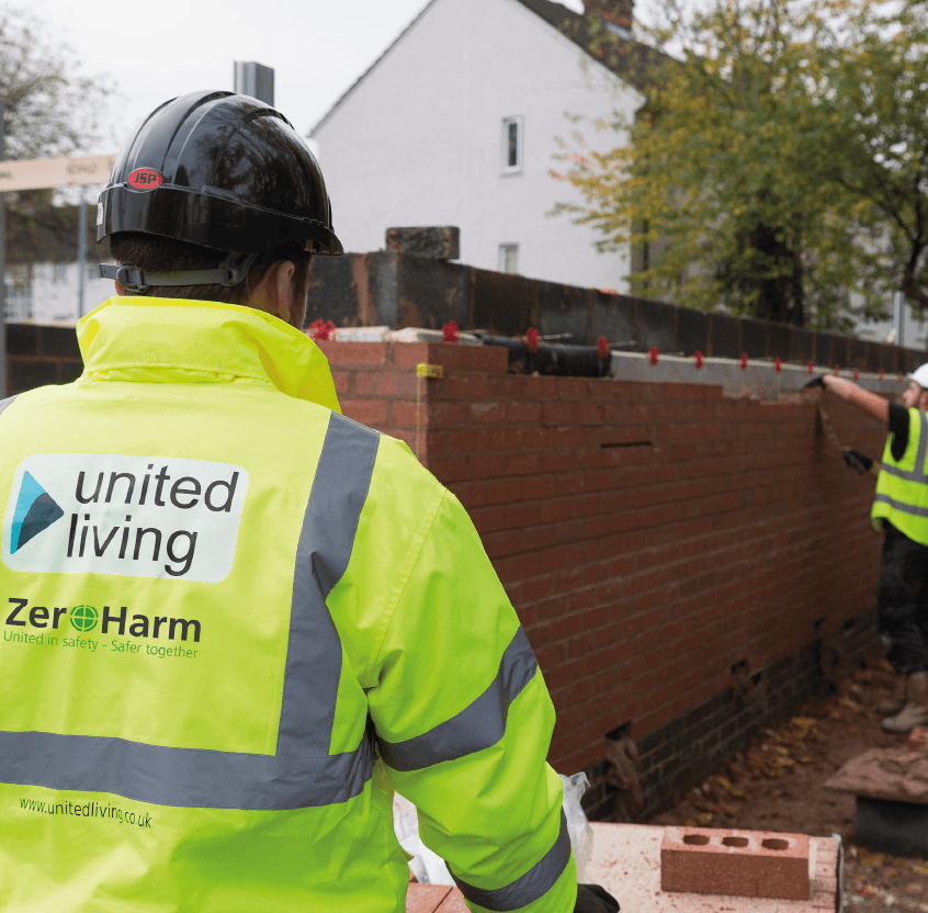 United Living construction worker on a site standing next to a brick wall