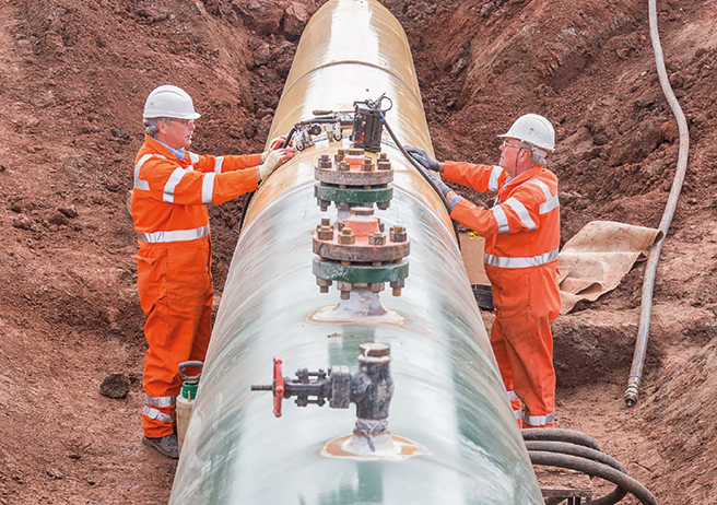 Two construction workers on site with large pipeline being laid in the ground